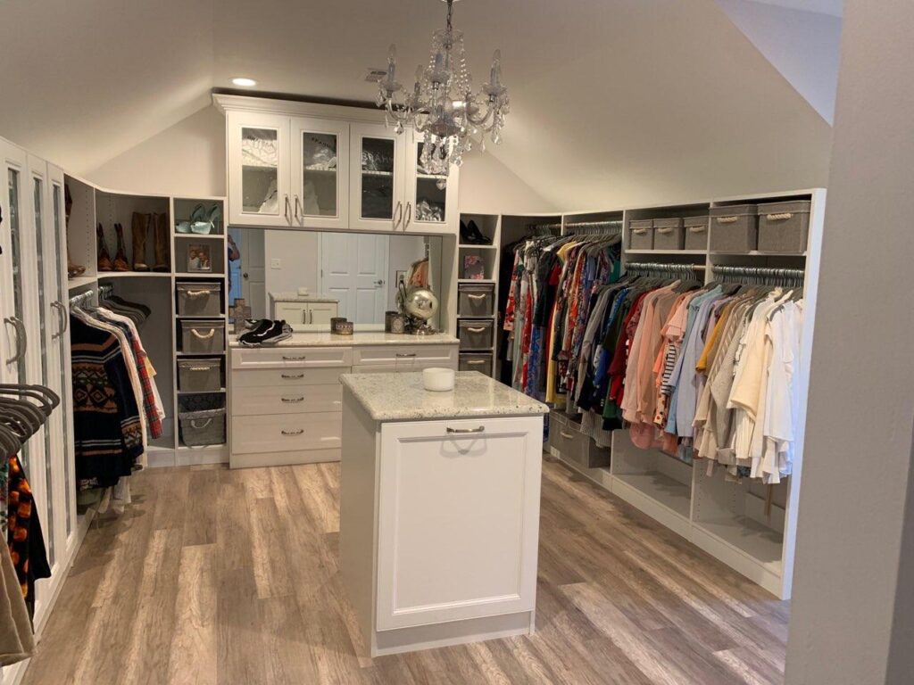 Cusom Closet With Shelves, Hanging And Shoe Cabinet To The Left, Hanging To The Right, A Bank Of Drawers And Cabinets On The Back And An Island With A Laundry Hamper And Marble Top In The Center.